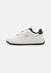 Zapatilla baja blanca con suela y detalles del talón en negro, cordones blancos y logotipo "Tommy Jeans" en el panel lateral.