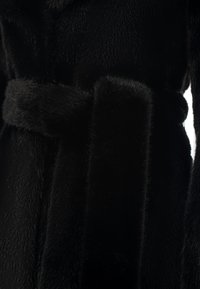 Primo piano di un cappotto di pelliccia nera con una cintura di pelliccia spessa legata in vita, che mette in evidenza la texture e la morbidezza.