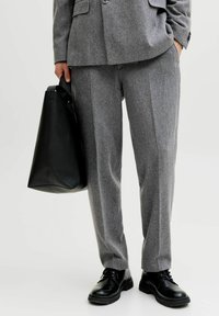 Grå ullbukser med skreddersydd passform, med frontfolder. Kombinert med blanke svarte snøresko og en strukturert svart handlenett.