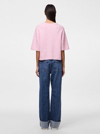 Camisola curta de malha cor-de-rosa com mangas curtas, combinada com jeans azuis de cintura alta com bainha desfiada e lavagem clara.