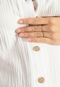 Witte, gestructureerde stof met verticale strepen, met houten knopen en een delicate gouden ring met kleine stenen op een hand.