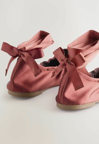 Ballerine in raso rosa con lacci coordinati e bordi scallopati. Le suole flessibili e la texture liscia aumentano il comfort.