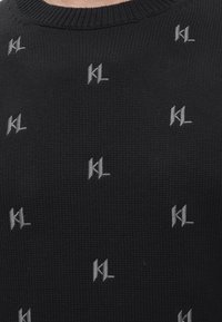 Tissu tricoté noir avec des initiales stylisées blanches "KL" répétées en petits motifs sur toute la surface.