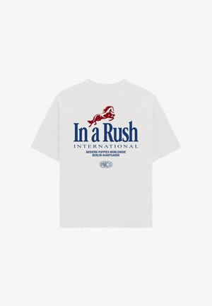 Witte T-shirt met korte mouwen en een rode paardenafbeelding boven grote blauwe tekst "In a Rush INTERNATIONAL" en kleinere tekst eronder.