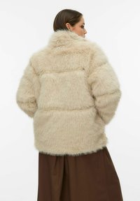 Beež värvusega kunstkarusnahast jakk kõrge kraega, langevate õlgade ja tekstuurse, pehme pinnaga. Tagaküljel on horisontaalne õmblusdetail.