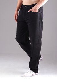 Schwarze Denim-Hosen mit geradem Schnitt, ausgestattet mit einem Knopfverschluss, fünf Taschen, heller Nähte und getragen mit weißen Sneakers.