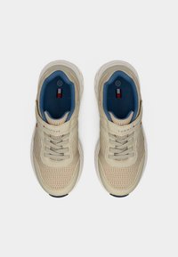 Μπεζ αθλητικά παπούτσια με επάνω μέρος από δίχτυ, κορδόνια και μπλε εσωτερική επένδυση. Διαθέτουν λογότυπο στο λουράκι και υφασμένο ελαστικό πάτο.