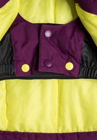 Doudoune avec un tissu jaune et violet éclatant, boutons-pression et texture douce. Les détails élastiques à l'ourlet ajoutent de la structure.