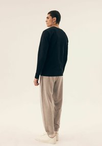 Schwarzes langärmliges Shirt, graue Sweatpants, weiße Sneakers. Einfaches Design, weicher Stoff, lockere Passform. Fokussierung auf die Kleidung von hinten.