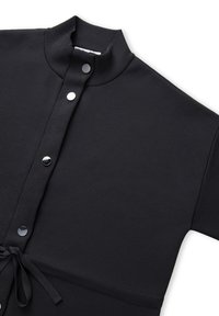 Zwarte kledingstuk met een hoge kraag, voorzien van zilveren drukknoopjes en een strikdetail in de taille. Gemaakt van een gestructureerde stof.