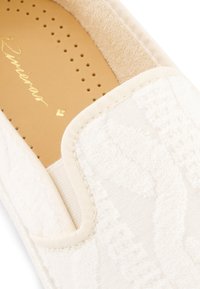 White slip-on shoe with textured fabric upper featuring a subtle pattern, leather insole, and stitched detailing along the edges.