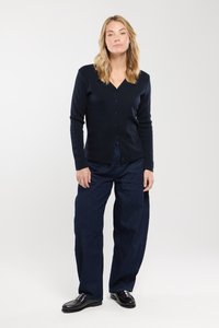 Granatowy kardigan z długimi rękawami i zapięciem na guziki, wykonany z gładkiego materiału. Połączony z luźnymi dżinsowymi spodniami i czarnymi butami.