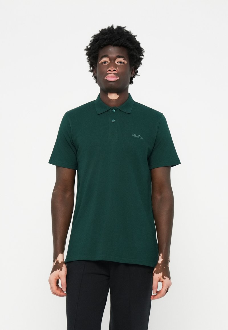 Polo de cor verde escura, feito de tecido texturizado, com uma pala de três botões e um pequeno logótipo bordado no lado esquerdo do peito.