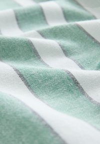 Pehme kangas rohelise ja valge triibulise mustriga, mis näitab tekstuuri ja õrnalt volditud kujul lähivaates.