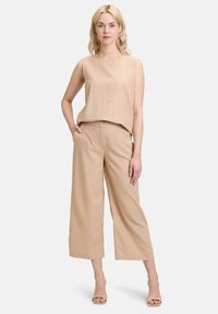 Beige ärmelloses Oberteil kombiniert mit beigen weit geschnittenen Hosen. Beide bestehen aus einem leichten Stoff und haben ein einfaches, lockeres Design.