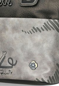 Bolso de mano de cuero negro con un fondo texturizado gris que presenta un acento floral, costuras blancas y un diseño con líneas curvas y letras.
