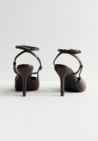 Sandali con tacco alto bordeaux, con punta chiusa, cinturino alla caviglia e tomaia in pelle testurizzata. Presentano un sottile tacco a stiletto e chiusura con fibbia.