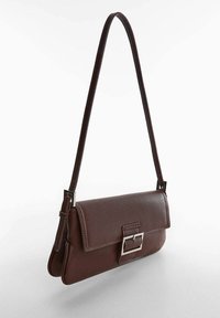 Brązowa skórzana torba na ramię z klapą i srebrną klamrą, z długim, regulowanym paskiem na jednolitym białym tle.