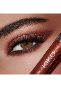 KIKO Milano vloeibare oogschaduw in een metallic kopertint, met een glanzende afwerking. Close-up van een bruine oog met sprankelende oogschaduw aangebracht.