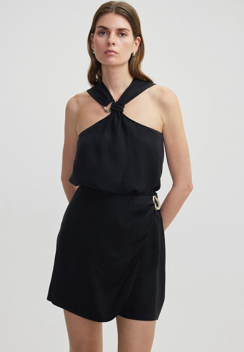 Schwarzes Oberteil-Kleid mit geknotetem Ausschnitt, drapierter Passform und seitlichem Schnallenakzent. Hergestellt aus leichtem Stoff mit glatter Textur.