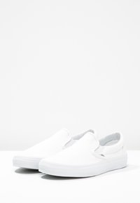 Baskets slip-on en toile blanche avec une texture lisse, bout arrondi, inserts élastiques sur les côtés et semelle en caoutchouc. Design minimaliste sans motifs.