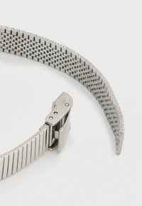 Ασημί μεταλλικό ρολόι με πλεκτό λουράκι από δίχτυ, που διαθέτει ασφαλές κούμπωμα. Το λουράκι έχει κομψό, λείο φινίρισμα και περιμετρικές άκρες.