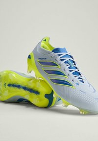 Chaussures de football Adidas Predator blanches et bleues avec semelles et crampons jaune néon, positionnées avec une chaussure reposant sur l'autre.