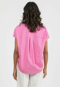 Blusa a righe rosa con maniche corte, tessuto fluido, dettaglio plissettato sulla schiena, orlo arrotondato e una texture liscia.