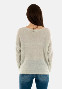 Suéter liviano de color crema tejido con un ajuste holgado y una trama abierta, combinado con jeans de mezclilla azul oscuro. Diseño simple y casual.