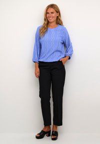 Lichtblauwe blouse met golvend kanten patroon, driekwart mouwen, gecombineerd met zwarte broek en zwarte open teen chunky hakken.