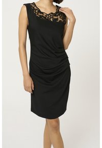 Robe noire sans manches, avec un col en dentelle, un tissu drapé et une silhouette ajustée. Elle présente une texture douce et une coupe à hauteur du genou.