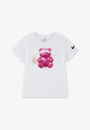 Λευκό παιδικό T-shirt Nike με κοντά μανίκια, με ροζ λογότυπο Nike swoosh και λαμπερό ροζ αρκουδάκι που φοράει κορδέλα και μπλουζάκι με το λογότυπο μπροστά.