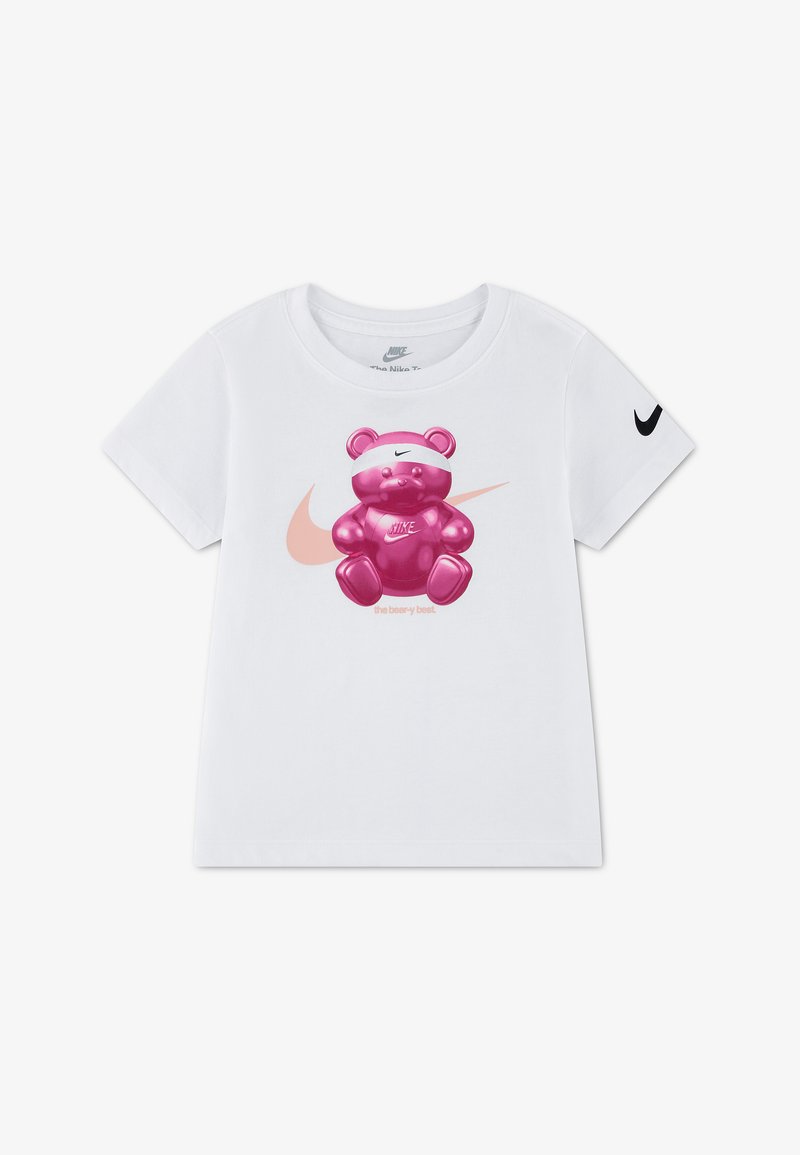 Λευκό παιδικό T-shirt Nike με κοντά μανίκια, με ροζ λογότυπο Nike swoosh και λαμπερό ροζ αρκουδάκι που φοράει κορδέλα και μπλουζάκι με το λογότυπο μπροστά.