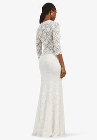 Weißes Spitzenkleid mit langen Ärmeln, taillierter Silhouette und floralem Muster. Der Rücken hat ein durchsichtiges Spitzenmuster und einen ausgestellten Saum.
