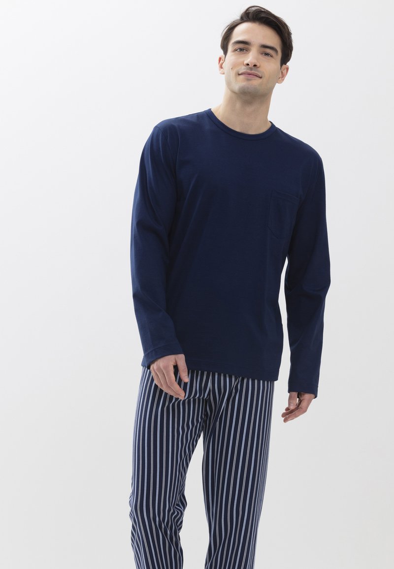 Camisa de manga larga azul marino con un bolsillo en el pecho, combinada con pantalones de pijama a rayas azul marino y blancas, que presentan un corte relajado y una tela suave.