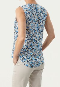 Bezrukávová květinová blůza s modrými a černými květinami na světlém pozadí, s kulatým lemem a detaily knoflíků na zadní straně.