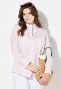 Camicia a maniche lunghe a righe rosa con colletto alto, abbinata a una borsa di paglia intrecciata con fiori e manici azzurri.