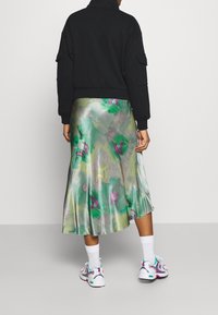 Svart fleece zip-up jacka, blommig satin kjol i gröna och lila toner, kombinerat med vita strumpor och färgglada sneakers, sedd bakifrån.