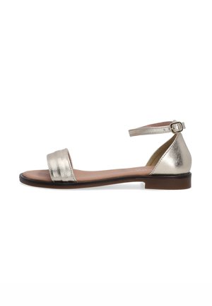 Plochá sandal s metalickým zlatým povrchem. Má široký přední pásek a kotníkový pásek se sponou. Plochá podrážka, minimalistický design.