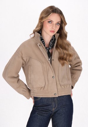 Vaahto beige-jakke on kauluksella, napilla ja etutaskuilla. Yhdistetty mustaan bandanaan, joka on käytetty tummien farkkujen kanssa.