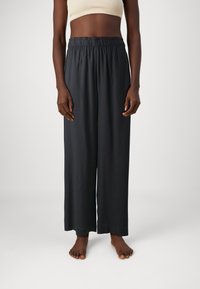 Pantalones anchos negros de tela suave, con cintura elástica y corte recto hasta el tobillo.