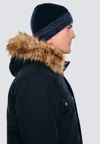 Granatowa parka z kapturem obszytym sztucznym futrem i kilkoma przednimi kieszeniami. Prążkowana dzianinowa czapka z kontrastowym poziomym paskiem na dole.