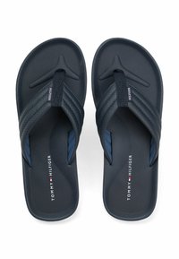 Un paio di infradito Tommy Hilfiger blu scuro con cinturini texturizzati e logo stampato sulla soletta, esposte su uno sfondo bianco.