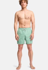 Pantaloni da nuoto verde menta con vita elasticizzata e cordoncino. Realizzati in tessuto leggero, presentano un design semplice e monocolore.