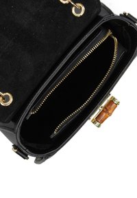 Borsa nera con pattina in suede, scomparti con zip, accessori in metallo dorato e chiusura in legno. Texture liscia e design strutturato.