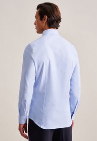 Camicia azzurra chiara a maniche lunghe in un tessuto morbido, con una vestibilità su misura, dotata di colletto con bottoni e dettagli bianchi sui polsini.