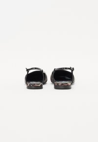 Sandales noires à dos ouvert avec un petit talon, présentant un design à imprimé léopard texturé sur la semelle et une bride de cheville ajustable.