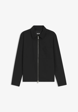 Veste noire à manches longues avec fermeture éclair et col, une poche poitrine et une fermeture éclair argentée visible, étiquetée « BOSS » à l’intérieur du col.