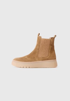 Tan suede ankle boot with ribbed elastic side panels, thick light brown ribbed sole, and pull tabs on front and back.