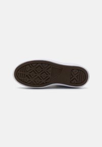 Semelle de sneaker blanche avec semelle extérieure en caoutchouc brun. Présente des motifs texturés pour l'adhérence, incluant des formes géométriques et le logo de la marque.